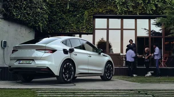 Grupo de quatro pessoas em frente a uma parede de vidro enquanto um veículo Škoda a carregar