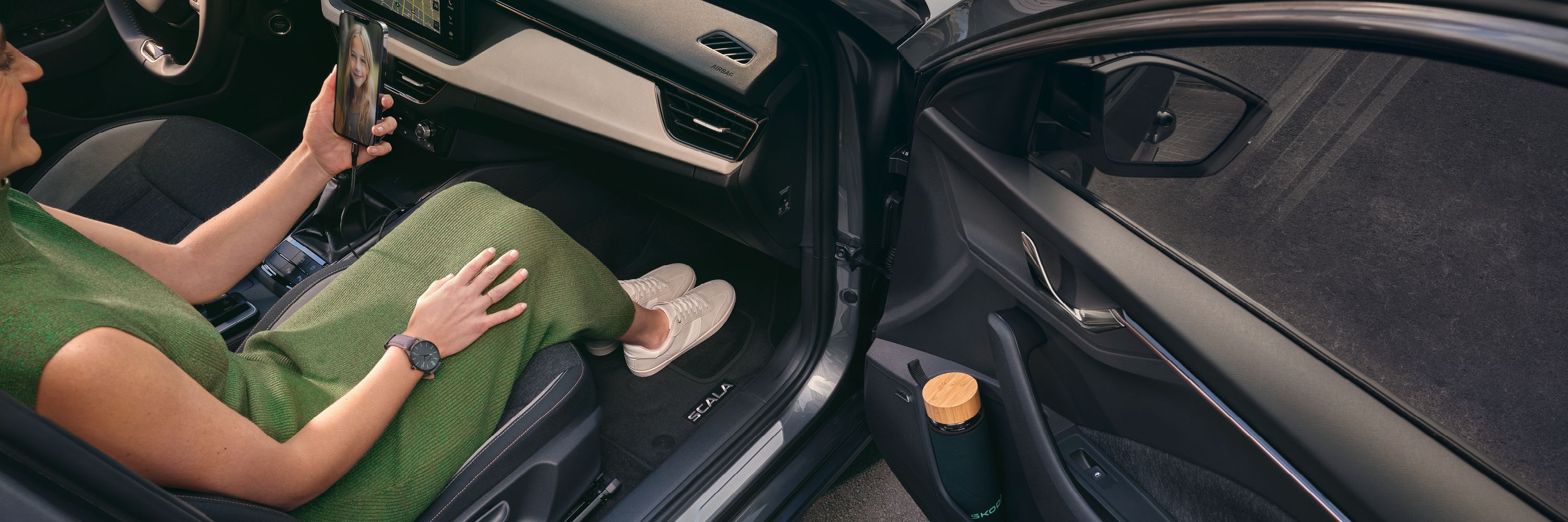 Eine Frau in einem Škoda Scala blickt auf ihr Smartphone.