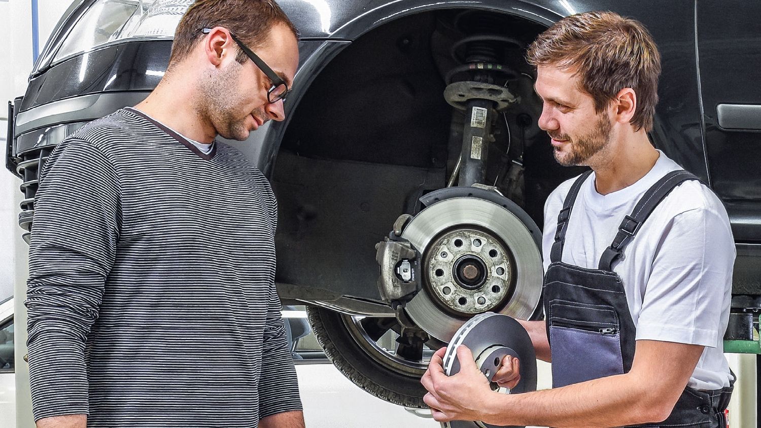 Ein Škoda Mechaniker in der Werkstatt zeigt einem Kunden die Bremsscheiben.