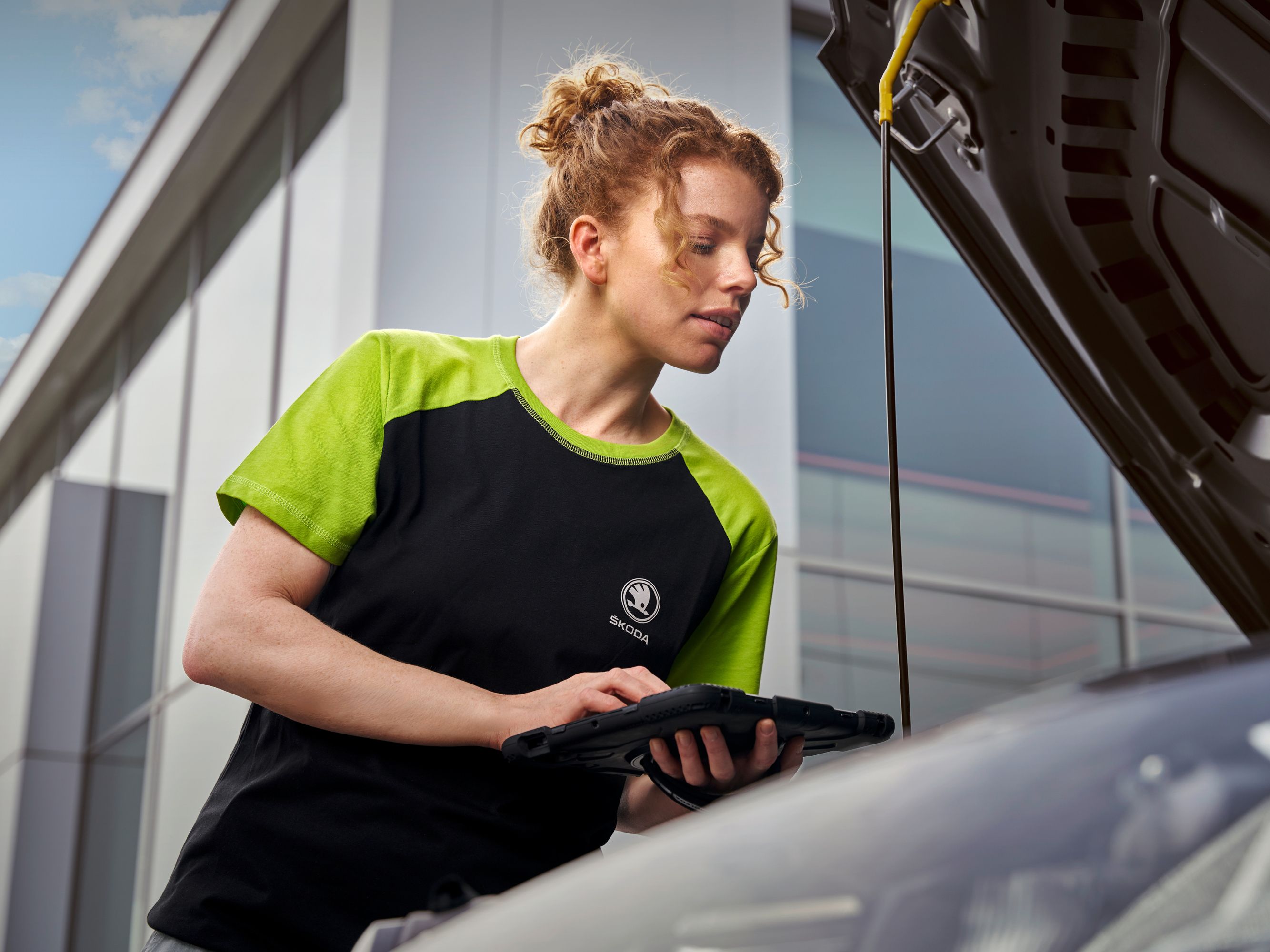 Eine Škoda Mechanikerin überprüft den Motor eines Škoda. Dabei tippt sie die Werte in ihr Tablet ein.
