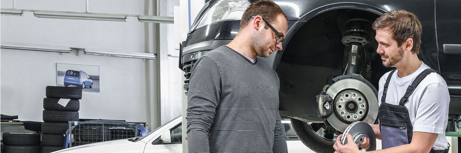 Ein Škoda Mechaniker in der Werkstatt zeigt einem Kunden die Bremsscheiben.