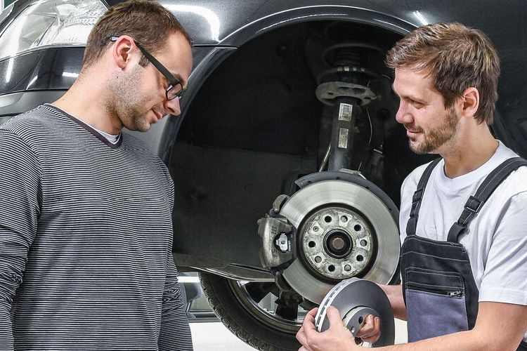 Ein Škoda Mechaniker in der Werkstatt zeigt einem Kunden die Bremsscheiben.