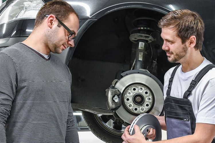 Ein Škoda Mechaniker in der Werkstatt zeigt einem Kunden die Bremsscheiben.