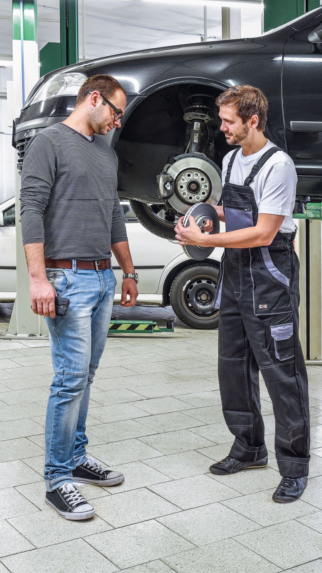 Ein Škoda Mechaniker in der Werkstatt zeigt einem Kunden die Bremsscheiben.